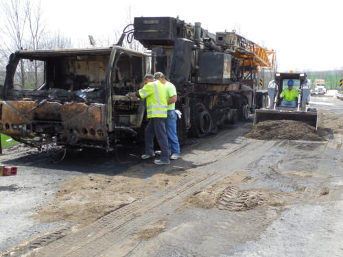 Crew assessing a burned commercial truck and absorbed spill residue at a roadside cleanup